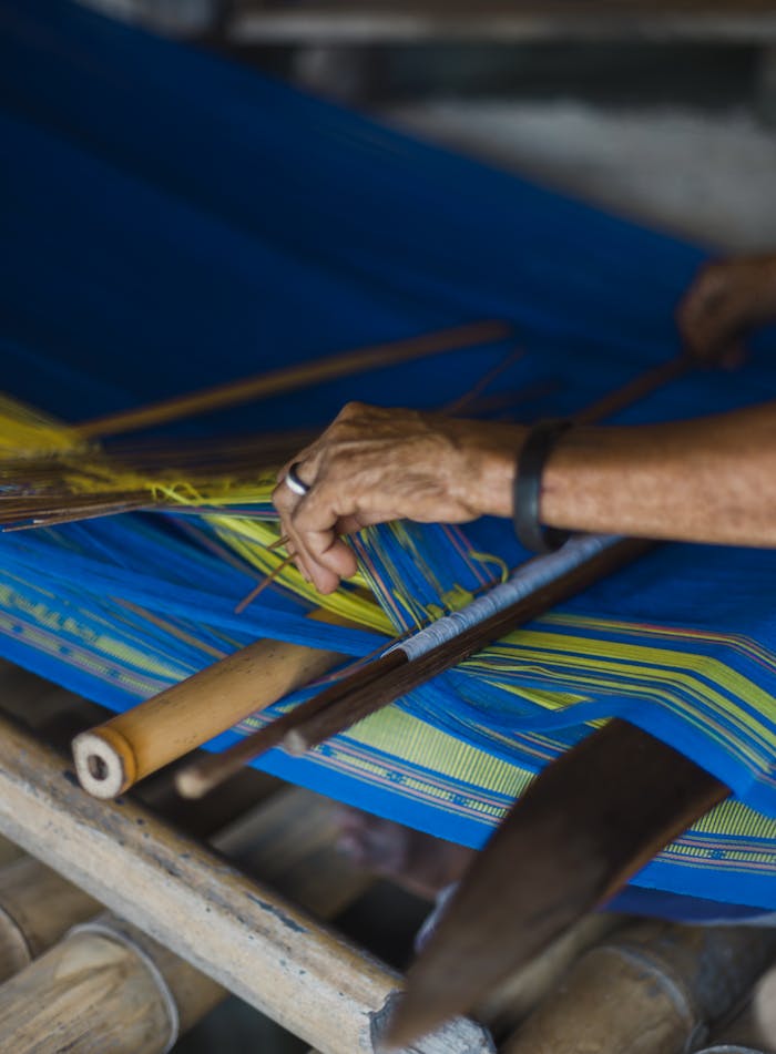 A close-up of a person's hands weaving colorful fabric on a traditional loom, demonstrating craft and skill.