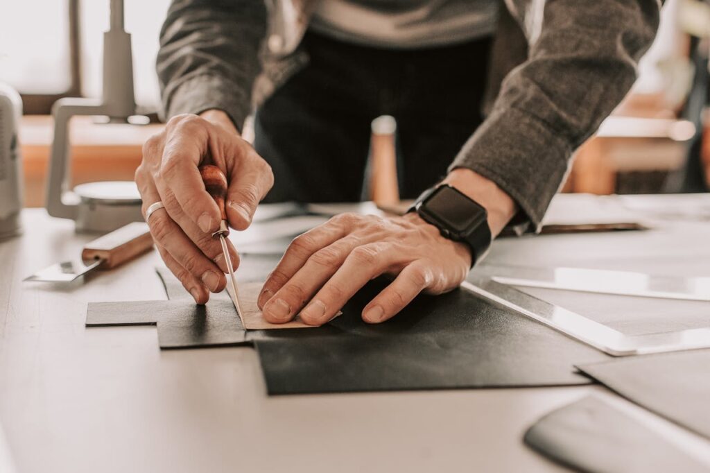 Artisan using an awl for handcrafted leatherwork in a workshop setting.